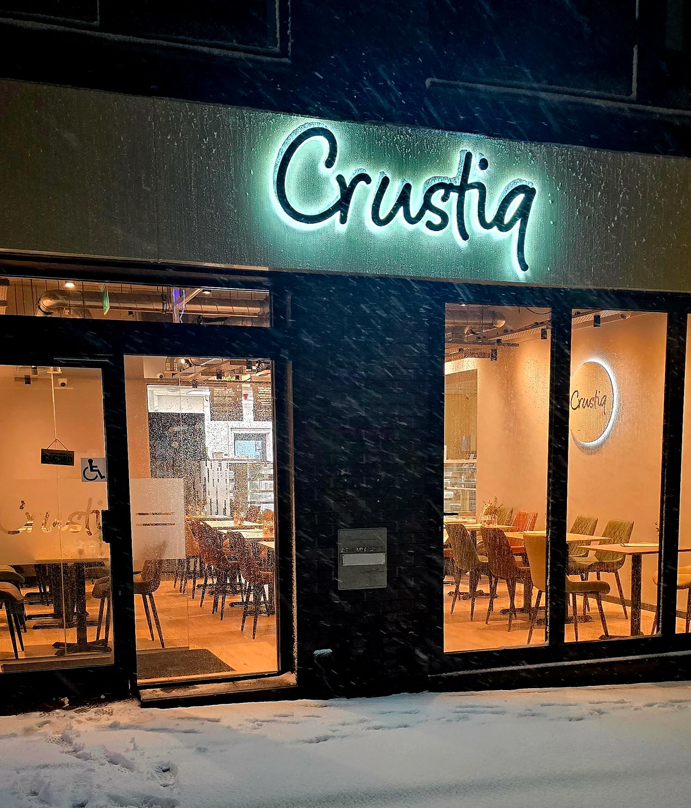 The illuminated Crustiq script sign and welcoming cafe entrance on a snowy evening