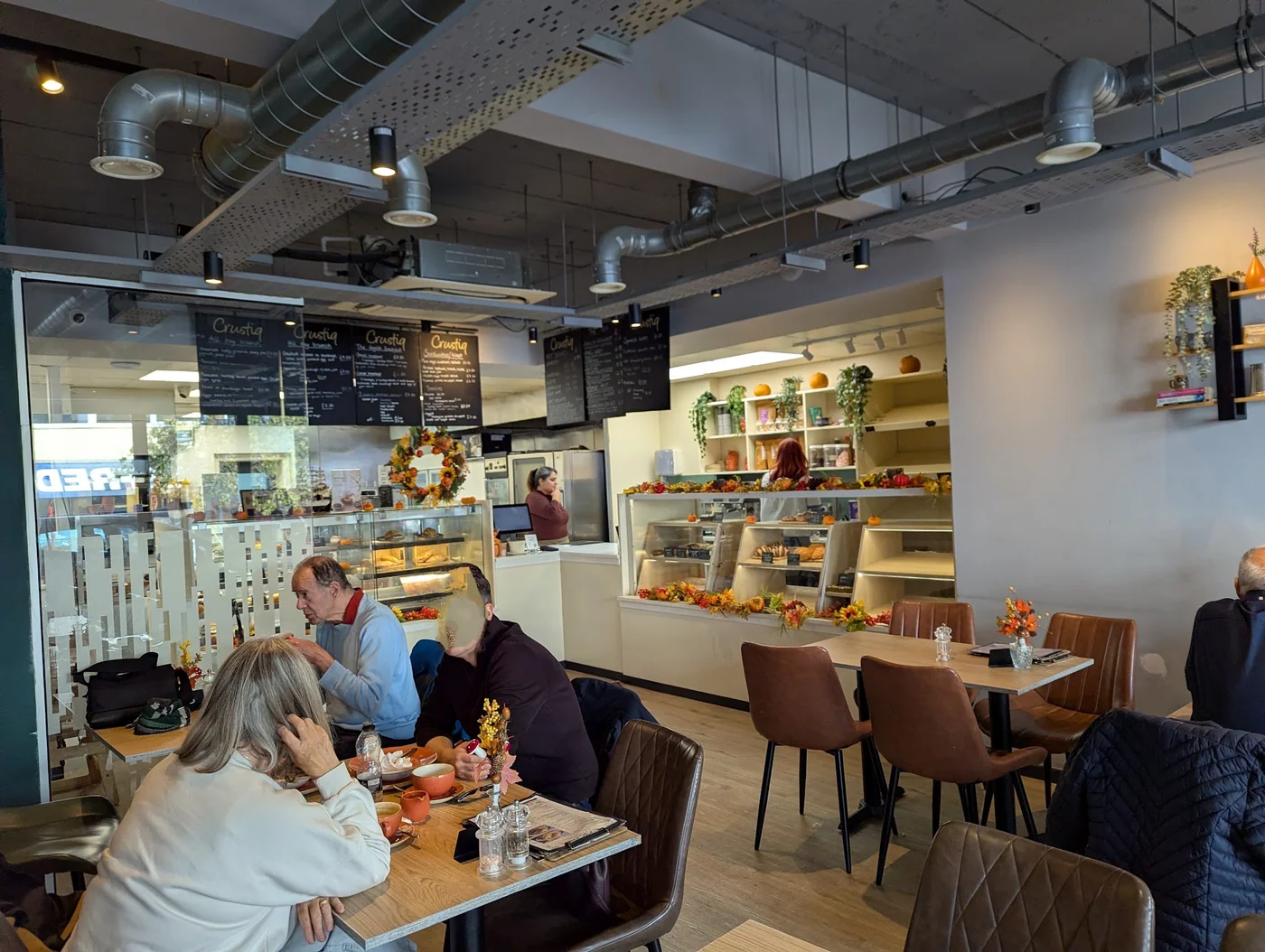 Customers enjoying the light cafe interior at Crustiq, with the bakery counter behind
